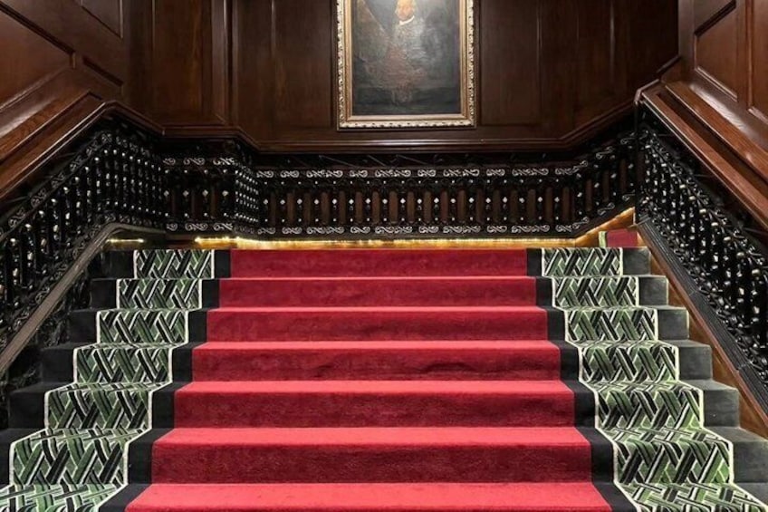 A grand staircase with red carpeted steps, wooden paneling, and decorative metal railings. 5