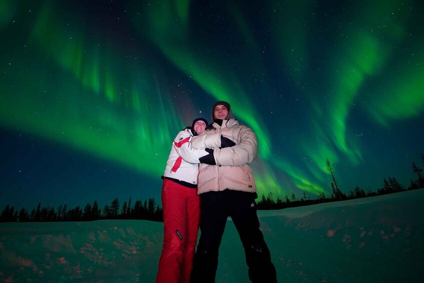 Two people standing on a snowy slope with the Northern Lights in the background. 2