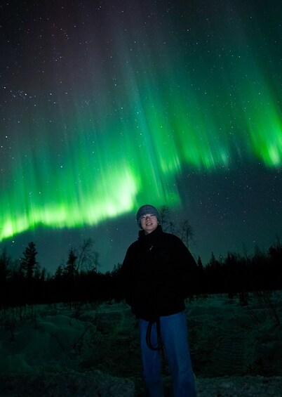 A person standing in a snowy landscape under a night sky with green aurora borealis. 1