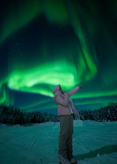 A person standing on snow-covered ground, pointing towards the night sky where the Northern Lights are visible. 3