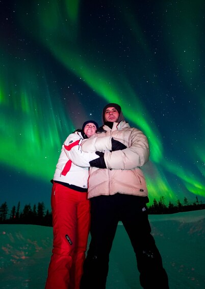 Two people standing on snow with the Northern Lights in the background. 2