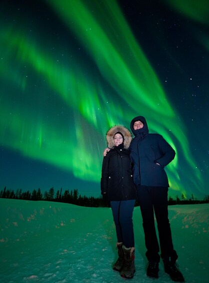 Two people standing on a snow-covered ground with the aurora borealis in the background. 5