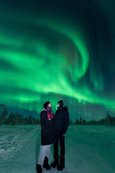 Two people standing on a snow-covered path under the Northern Lights. 3