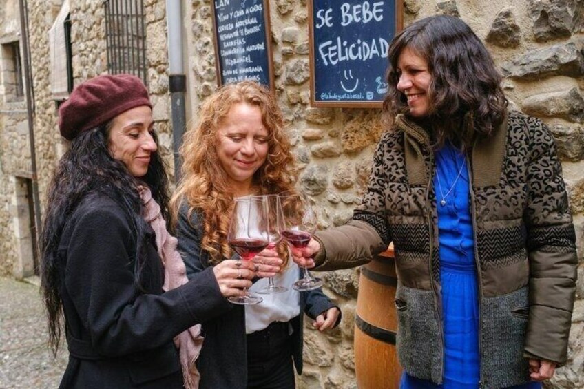 Three people holding wine glasses in front of a stone building with a sign that says 'SE BEBE FELICIDAD.' 5