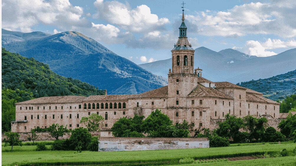A historic church with a bell tower, surrounded by lush greenery and mountains. 1
