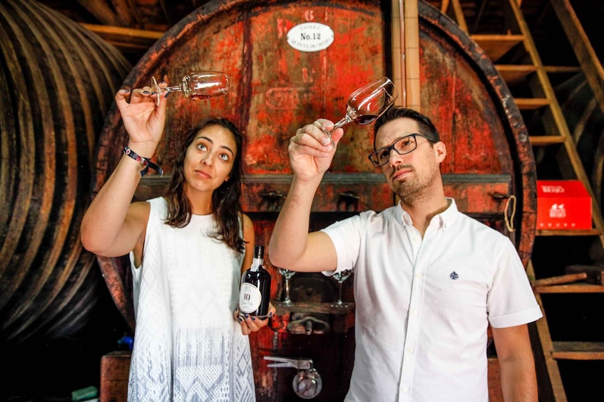Two people holding wine glasses in front of a large, rusted barrel with a label 'No. 12'. 1