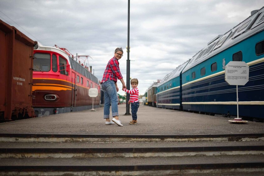 A person and a child standing on a train platform with trains in the background. 5