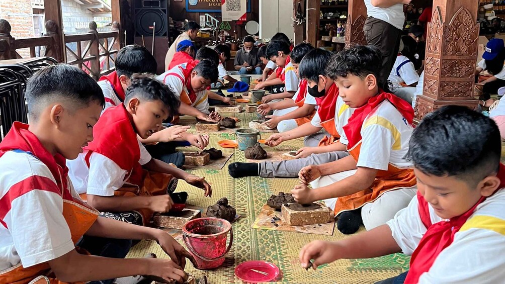 Children engaged in a craft activity, seated on a mat in a room with wooden furniture and decorative elements. 2