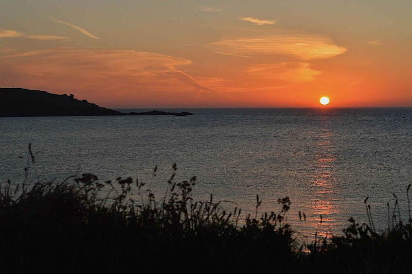 A sunset over a calm sea with silhouettes of land and vegetation in the foreground. 1