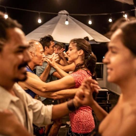 A group of people dancing in a circle under a tent with string lights. 4
