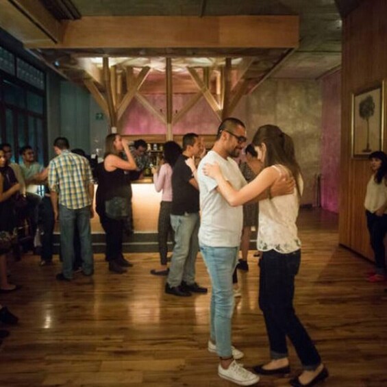 A dance floor with people dancing, wooden beams on the ceiling, and a bar area in the background. 3