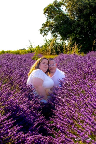 Two people in a field of purple flowers, possibly lavender, with trees in the background. 4