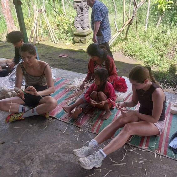 A group of people sitting on mats outdoors, engaged in an activity with straw. 2