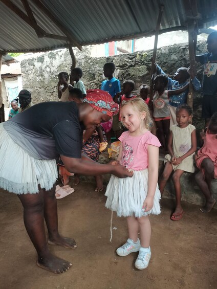 A person assisting a child with shoes under a corrugated metal roof. 2
