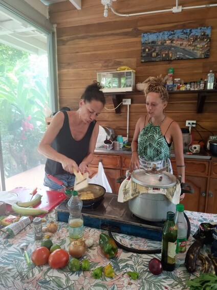 Two people cooking in a kitchen with a wooden interior, a window, and various cooking utensils and ingredients on the counter. 5