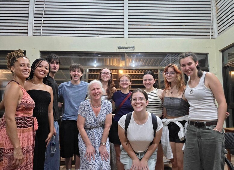 A group of people standing indoors with a metal roof and windows in the background. 2