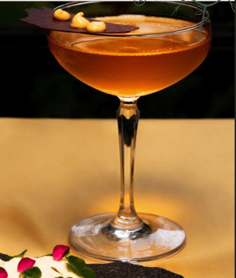 A cocktail in a stemmed glass with a garnish, set against a warm-toned background. 1