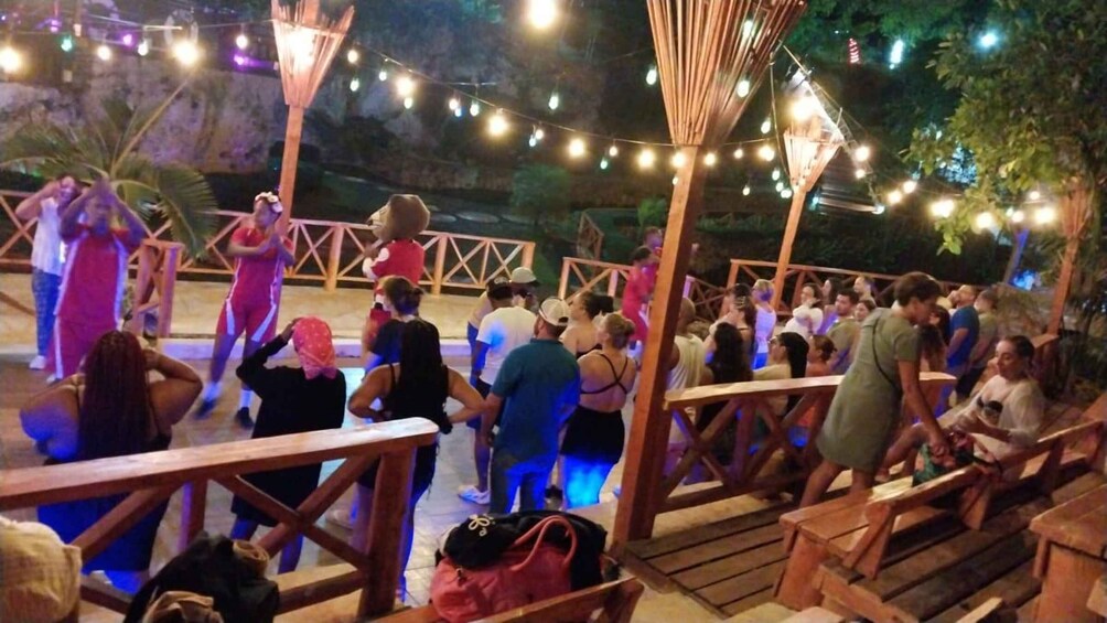 A group of people gathered at an outdoor event with string lights and wooden structures. 3