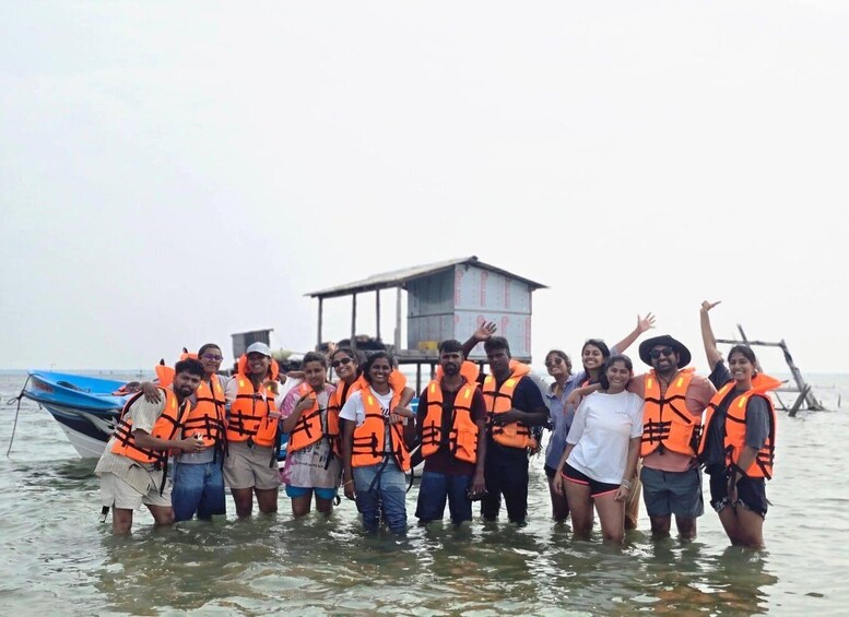 A group of people in orange life vests standing in shallow water near a boat and a wooden structure. 2