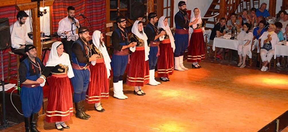 A group of people in traditional costumes performing on a stage with an audience seated at tables. 3