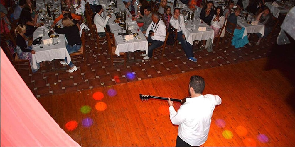 A man playing guitar on a stage with a crowd seated at tables in the background. 5
