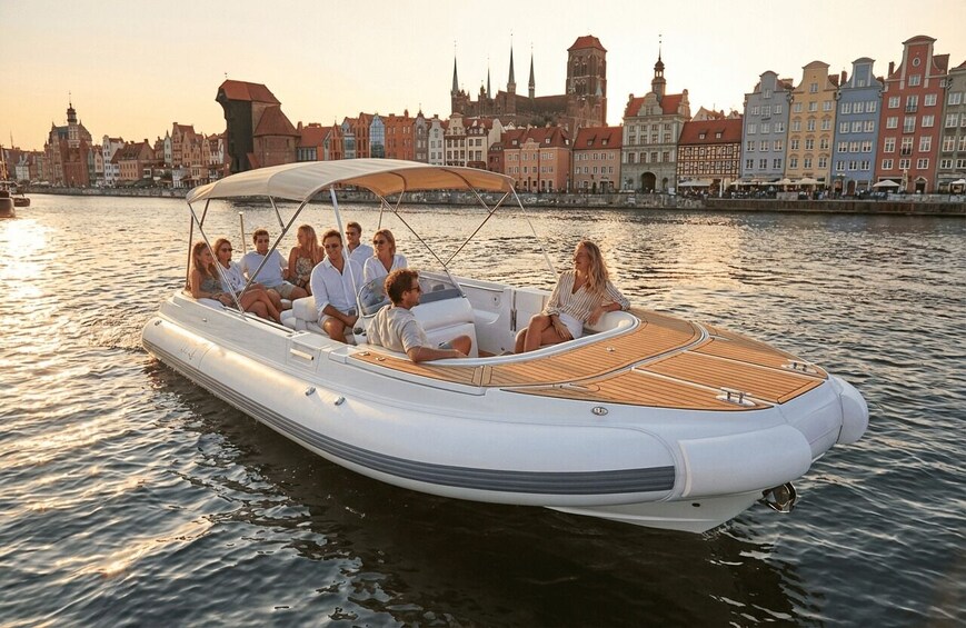 A group of people on a white motorboat with a wooden deck, cruising on a river with historic buildings in the background. 1