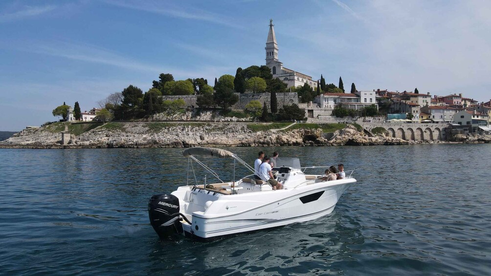 A white boat with a Mercury outboard motor on calm water, a rocky shoreline with buildings and a church in the background. 2