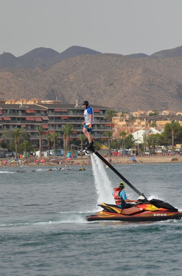A person jet-skiing on water with a jet ski, a beach, and buildings in the background. 3
