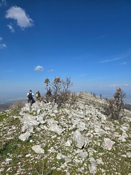 Two hikers on a rocky mountain trail with a clear blue sky. 2