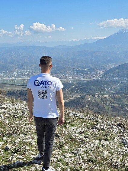 A person walking on a rocky mountain path with a scenic view of a valley and mountains in the background. 3