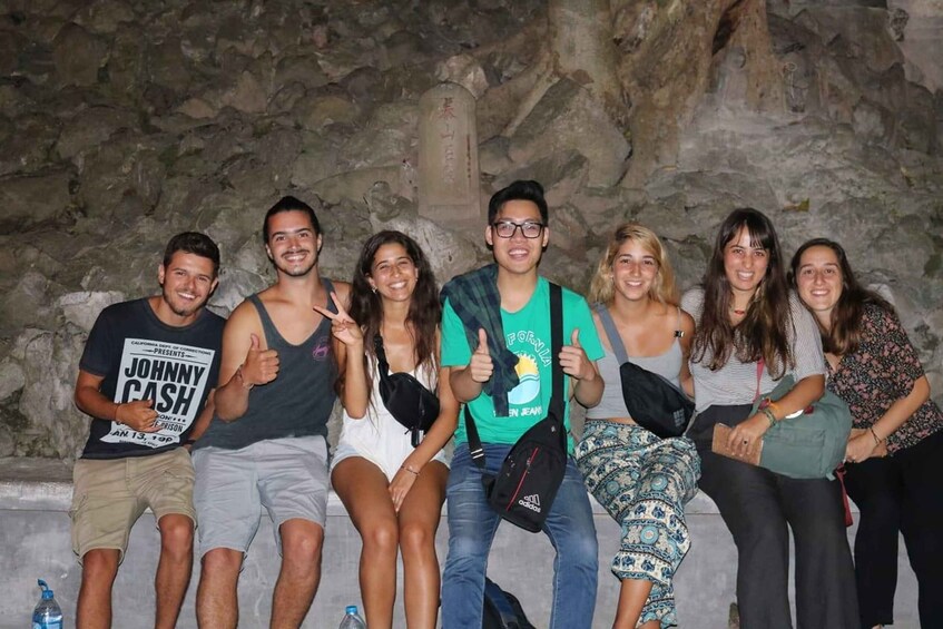 A group of people sitting on a stone wall with a cave-like background. 1