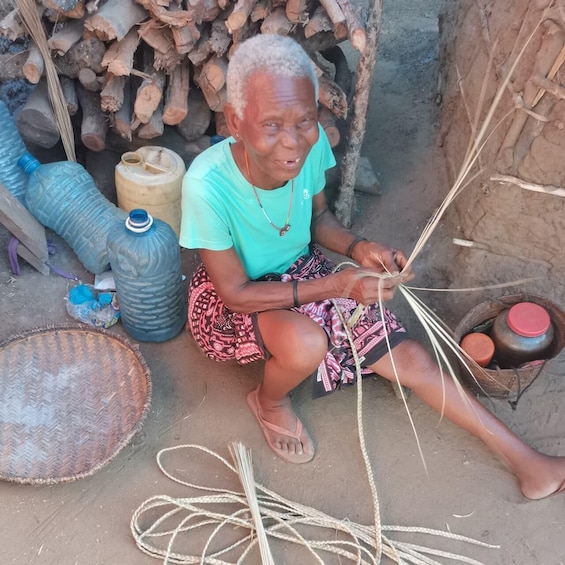 An elderly person sitting on the ground, weaving with a spindle. 1