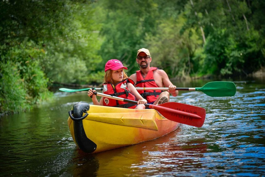 Two people in a yellow and black kayak on a river surrounded by greenery. 3