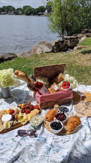 A picnic setup with a variety of cheeses, fruits, and pastries by a lakeside. 2
