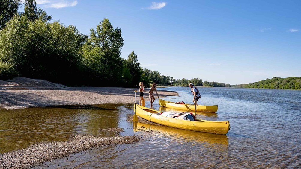 Three people in canoes on a calm river, surrounded by trees and a clear sky. 1