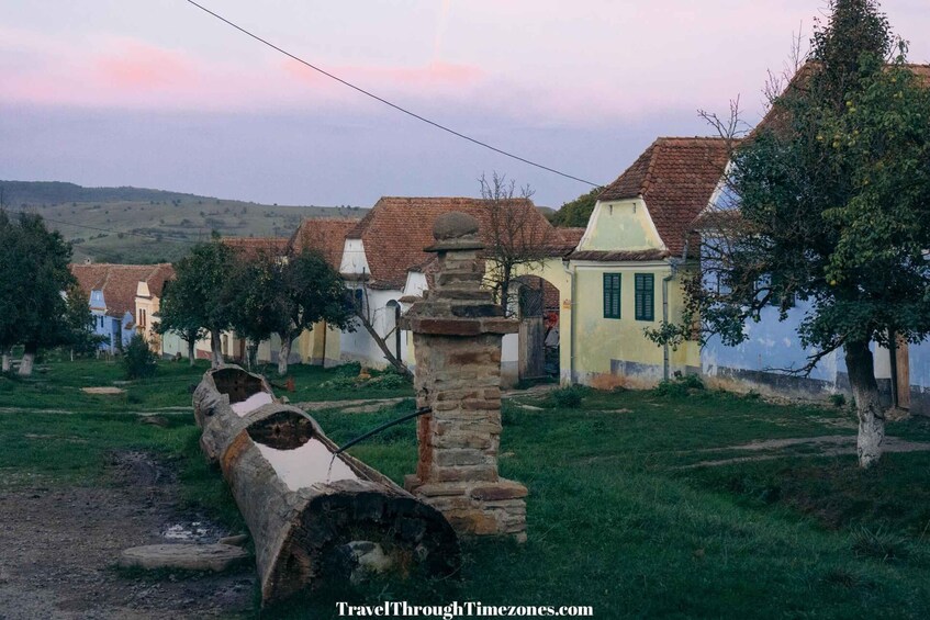 A rural village with traditional houses, a stone pillar, and a log in the foreground. 2