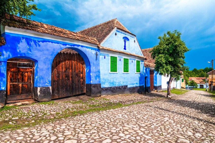 A cobblestone street with a blue building featuring green shutters and a wooden door. 3