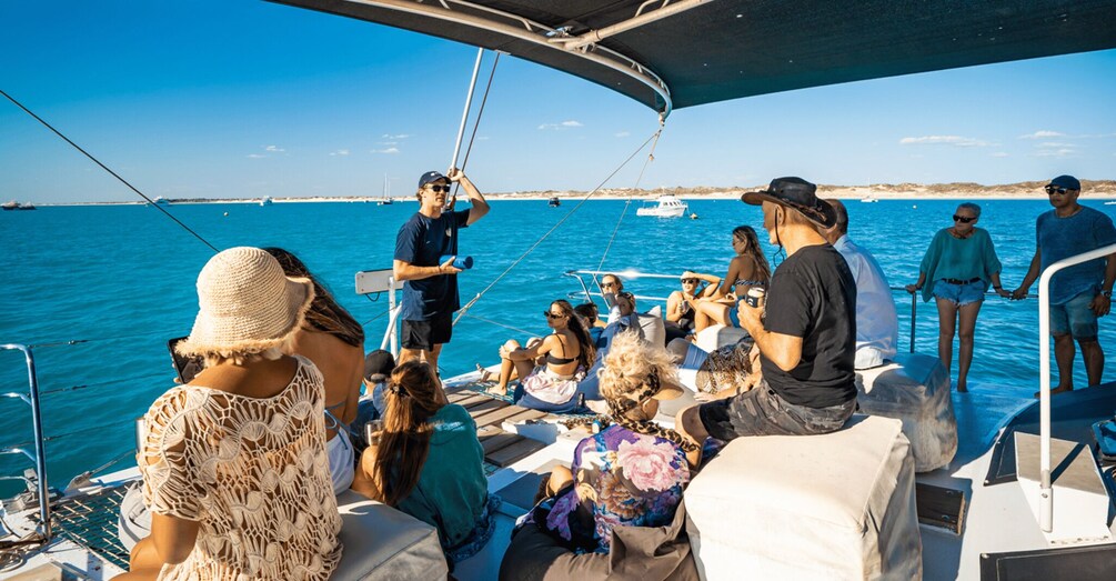 A group of people on a sailboat with a clear blue sea and distant land in the background. 2