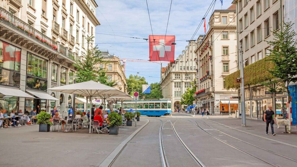 A tram on tracks, a red cross flag, and buildings with balconies. 2