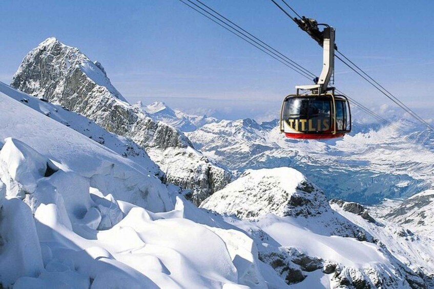 A cable car labeled 'TITLIS' ascending a snowy mountain ridge. 1