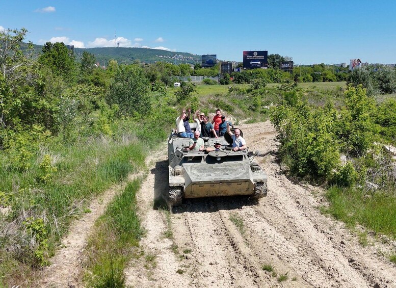 A group of people on a military vehicle driving on a dirt road surrounded by greenery. 4