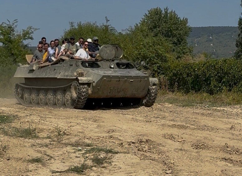 A military tank with soldiers on top driving on a dirt road. 5