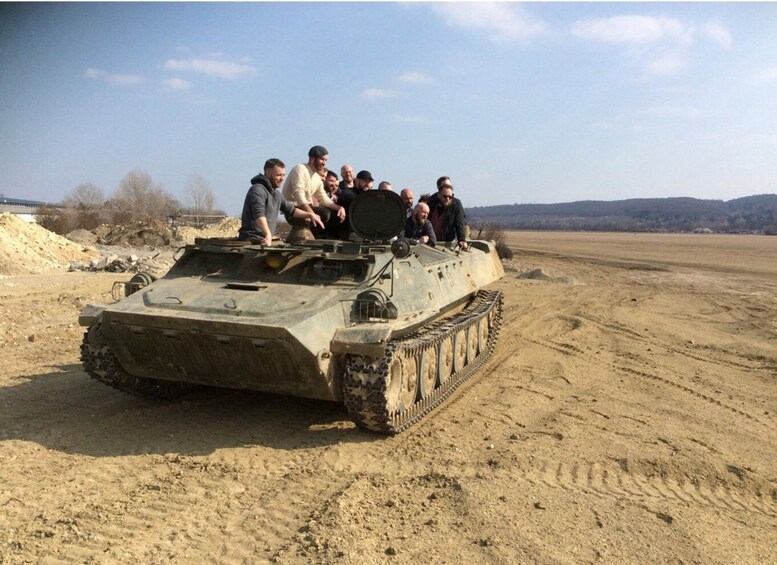 A group of people sitting on a military tank in a desert landscape. 1