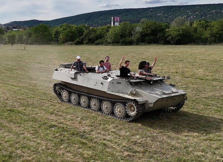 A military tank with four people on it in a grassy field with hills in the background. 1