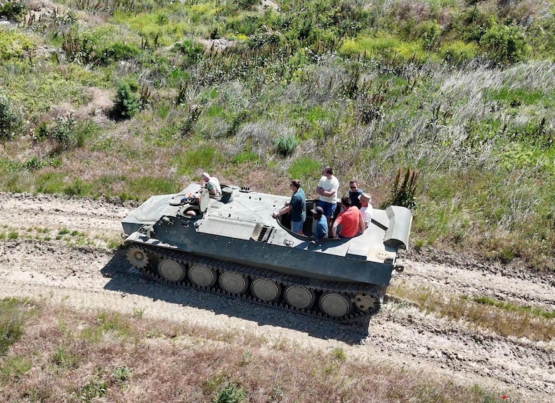 A military tank with soldiers on top, traversing a dirt path in a natural, green landscape. 2