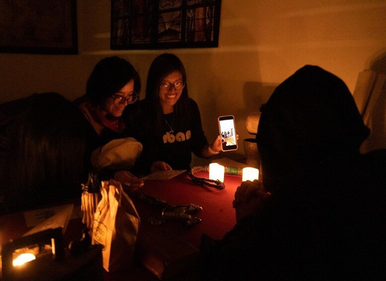 Three people sitting at a table with candles, one holding a smartphone. 1