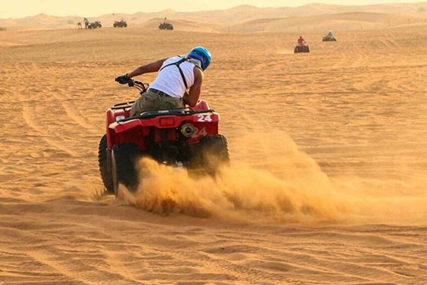 A person riding a red ATV in a desert with sand being kicked up. 1