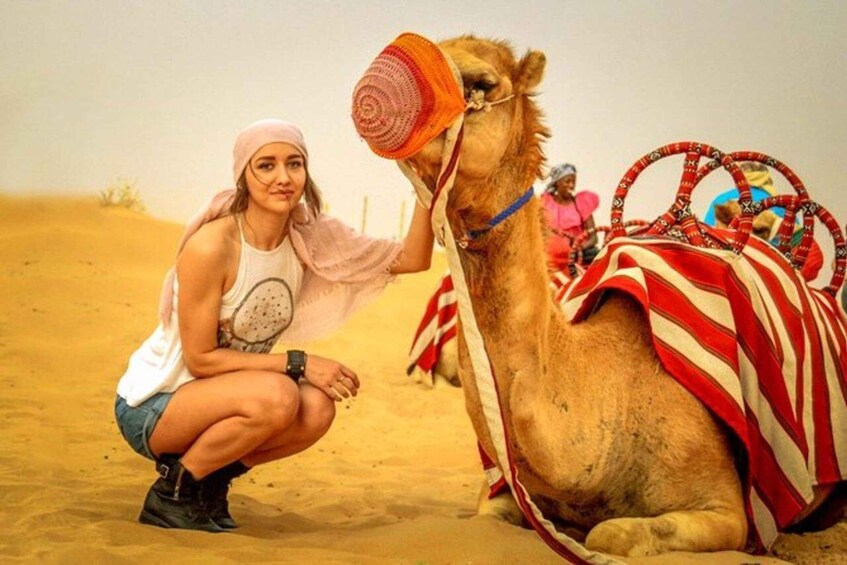 A person crouching next to a camel in a desert setting. 2