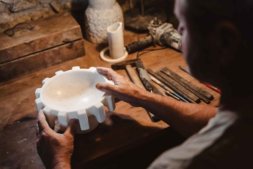 A person working with a white ceramic object on a wooden table. 1