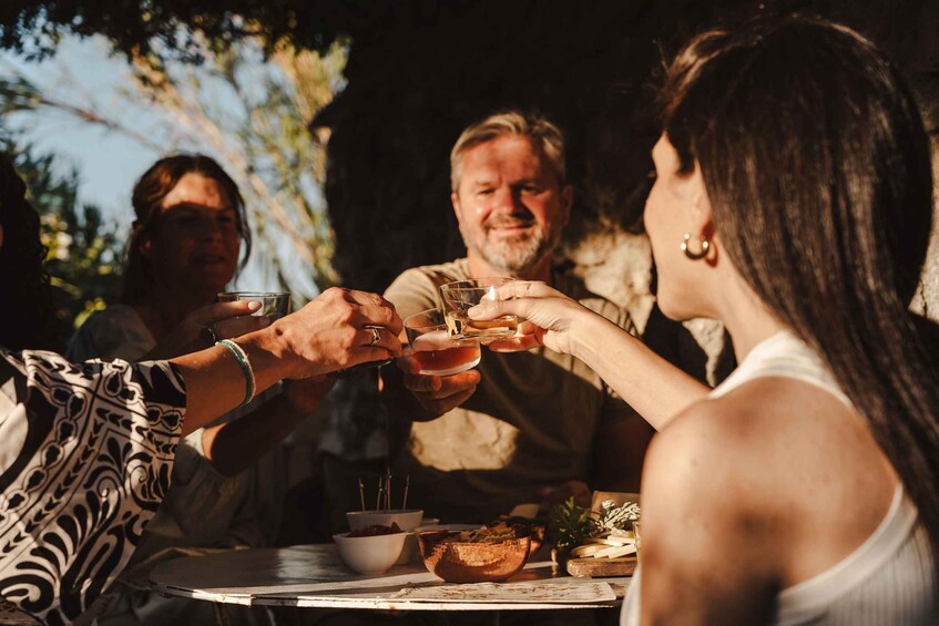 People toasting with drinks at an outdoor table with food and a candle. 2